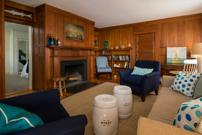 Photo showing a wood paneled living room with tan couch, blue chairs, and fireplace.